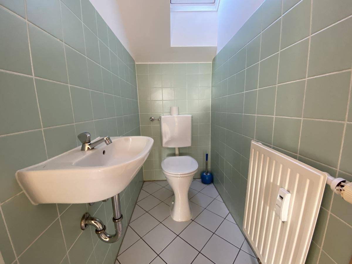 Kleines Gäste-WC mit hellgrünen Wandfliesen, Waschbecken, Toilette und einem Dachfenster.