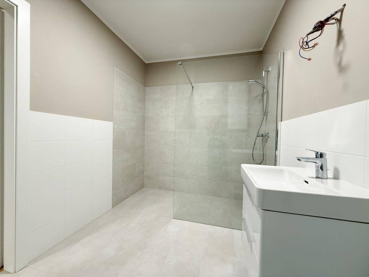 Helles Badezimmer mit großer Dusche, modernem Waschbecken und hellen Fliesen.