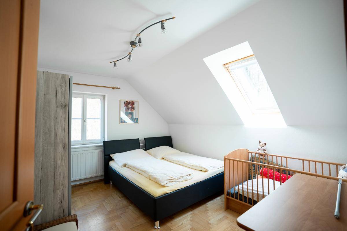 Helles Schlafzimmer im Dachgeschoss mit Doppelbett, Babybett und Dachfenster.