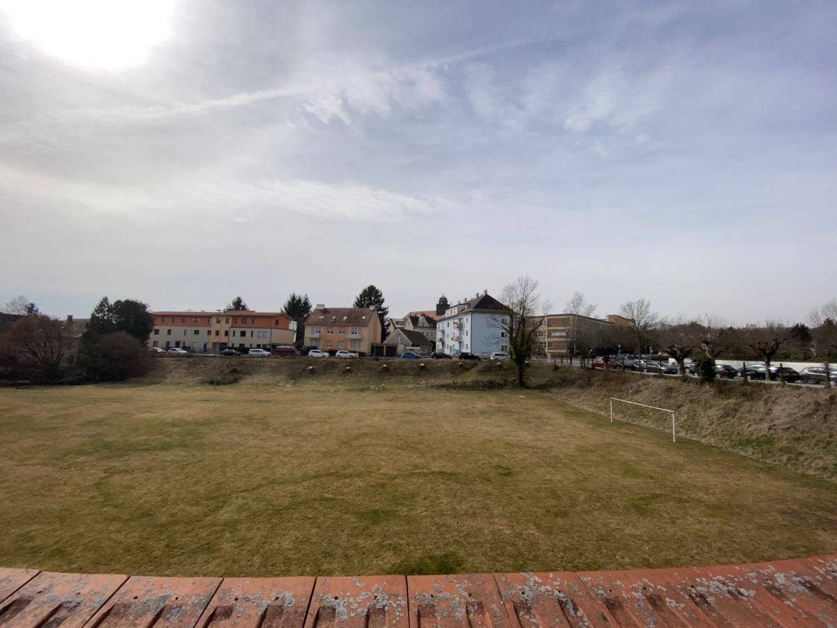 Weite Grünfläche mit einem Fußballtor und Blick auf eine Reihe von Gebäuden in der Ferne unter bewölktem Himmel.