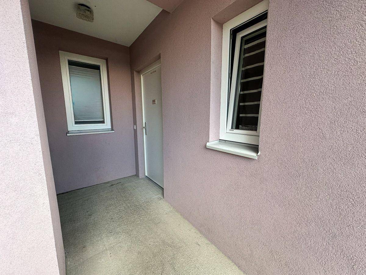 Eingangsbereich eines Gebäudes mit rosa Fassade und zwei Fenstern.