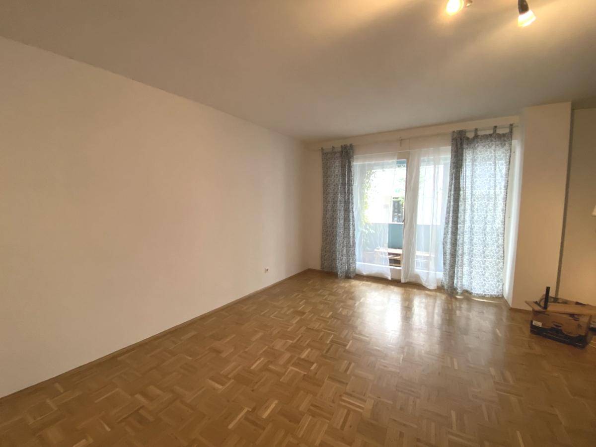 Geräumiges Wohnzimmer mit Parkettboden, viel Tageslicht und Zugang zum Balkon.