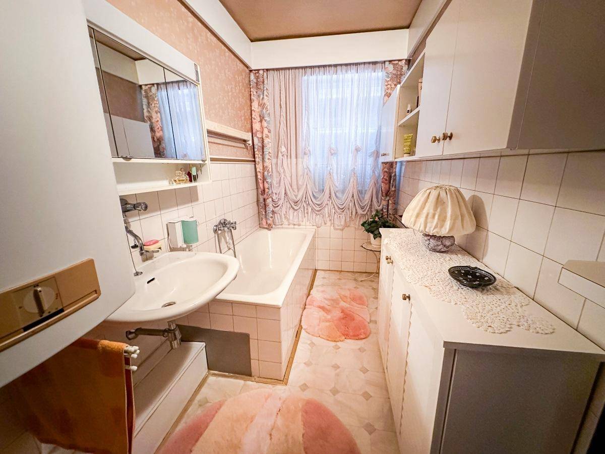 Badezimmer mit Badewanne, Waschbecken und rosa-beigen Fliesen im Vintage-Stil.