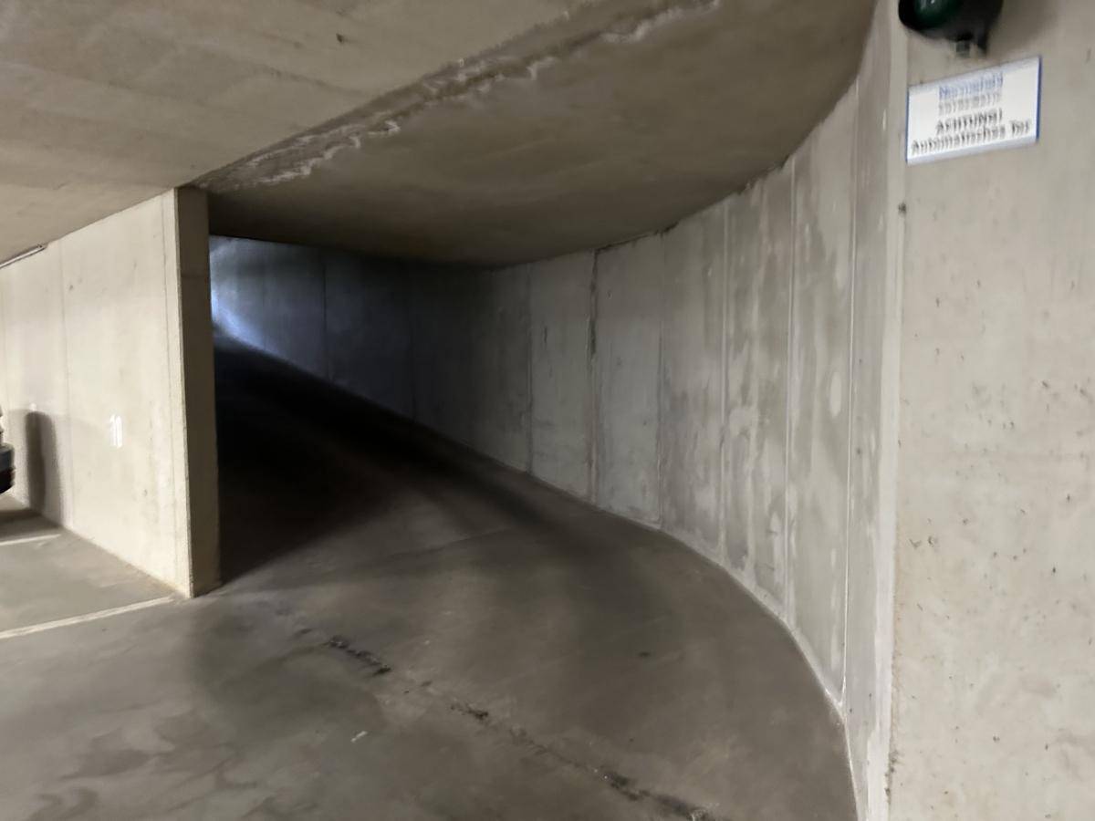 Gebogene Betonrampe führt in eine Tiefgarage mit automatischem Tor.