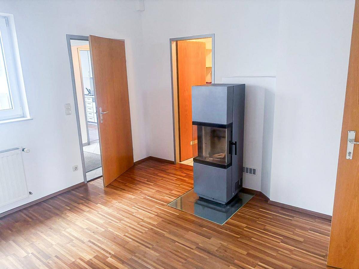 Heller Büroraum mit Holzboden und einem freistehenden Kaminofen als zentrales Element.