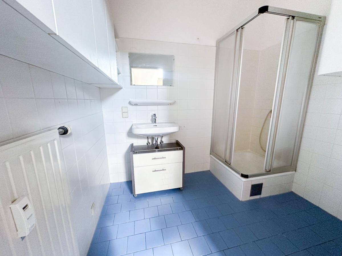 Badezimmer mit Dusche, Waschbecken und blauen Bodenfliesen, ausgestattet mit einem Heizkörper.