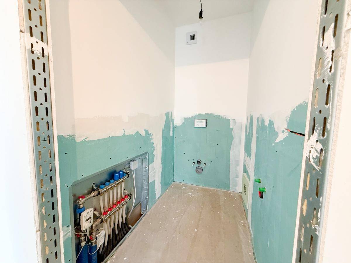 Badezimmer im Rohbau mit sichtbaren Sanitärinstallationen und Unterputzverteiler für Heizung.
