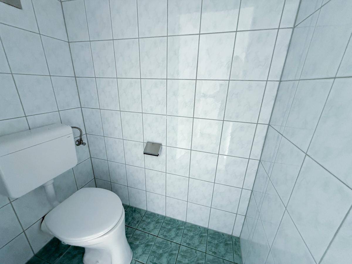 Kleines Gäste-WC mit hellblauen Fliesen an Wänden und Boden sowie einer einfachen Toilette.