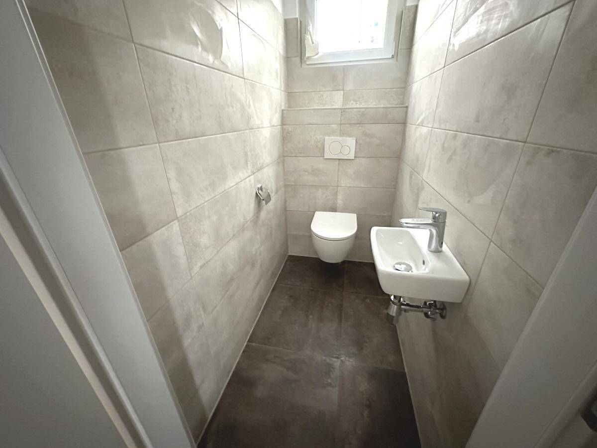 Kleines Gäste-WC mit Wand-WC, Handwaschbecken und Fenster, komplett gefliest.