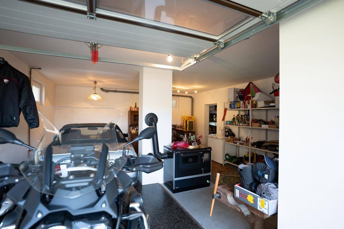 Geräumige Garage mit Motorrad, Auto und Regalen für diverse Lagerungsmöglichkeiten.