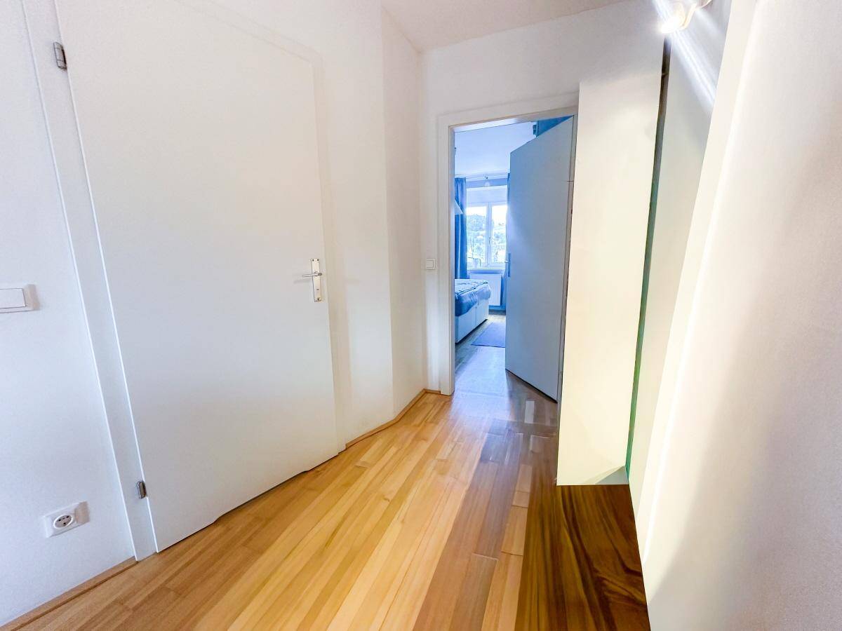 Heller Flur mit Holzboden und weißen Türen, der zu einem Schlafzimmer führt.