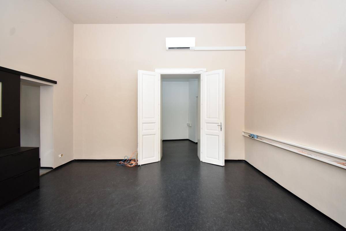 Leerer Büroraum mit hohen Decken, Klimaanlage und einer Doppeltür, die zu einem weiteren Raum führt.