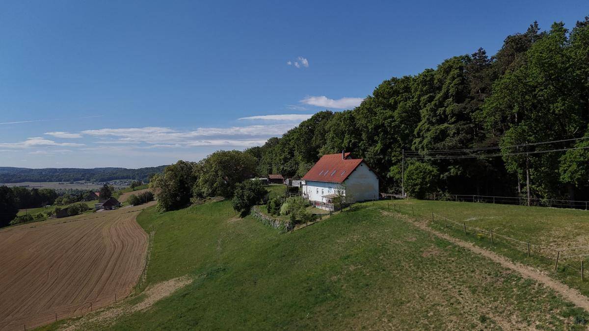 Idyllisches Einfamilienhaus mit rotem Dach auf einem grünen Hügel am Waldrand mit weitem Blick.