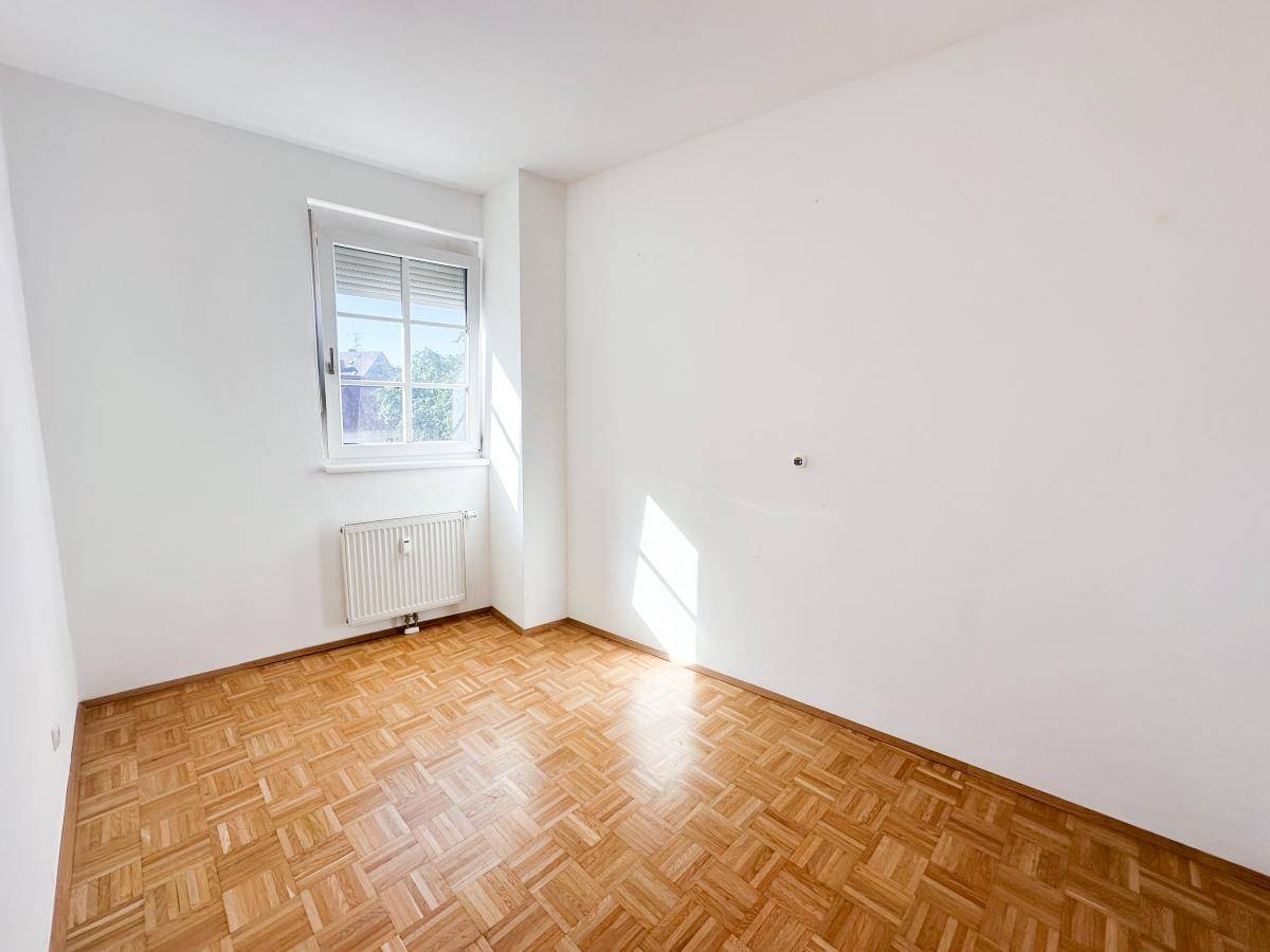 Helles Zimmer mit Parkettboden und Fenster, das viel Sonnenlicht hereinlässt.