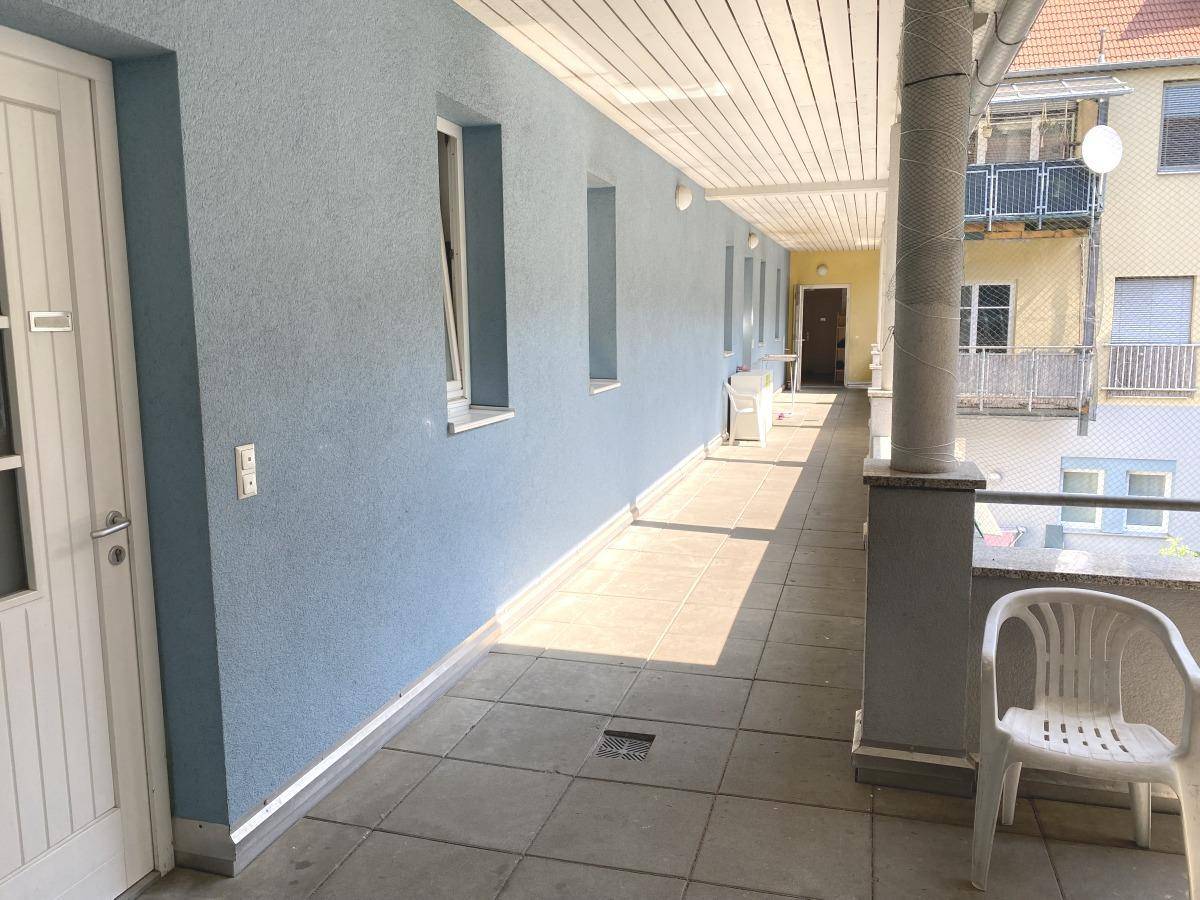 Überdachter Außenbereich mit blauer Fassade, Fliesenboden und Blick auf die Umgebung.
