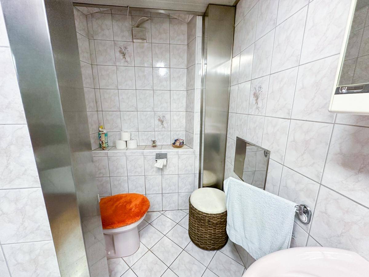 Separate Toilette mit hellen Fliesen und einem kleinen Waschbecken.