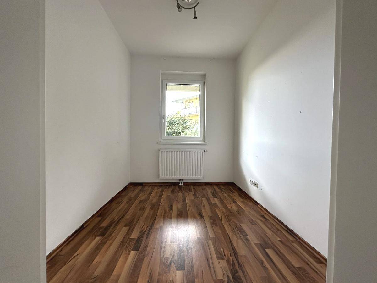 Helles Schlafzimmer mit Laminatboden und einem Fenster, das den Blick ins Grüne freigibt.