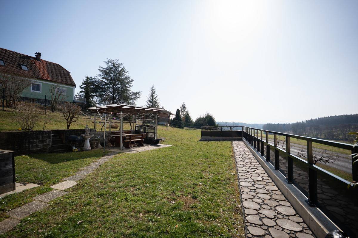 Gepflegter Gartenbereich mit Rasenfläche, Steinweg und überdachtem Sitzbereich.