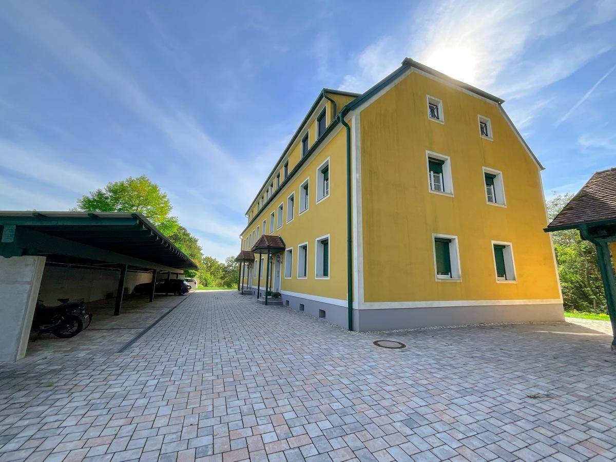 Ansicht des Wohngebäudes mit Parkplätzen und Carport unter blauem Himmel.