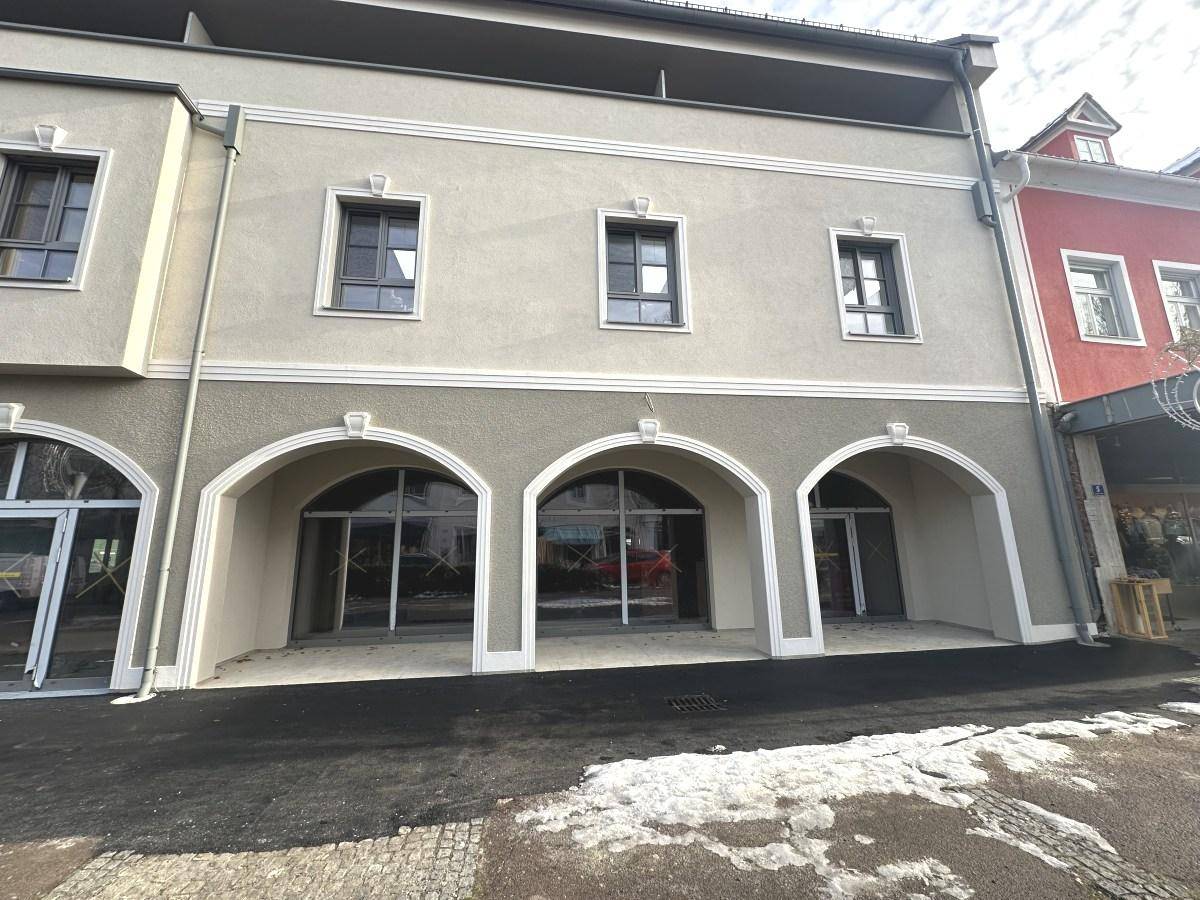 Fassade eines modernen Gebäudes mit eleganten Bogenfenstern im Erdgeschoss und gepflegter Putzfassade.