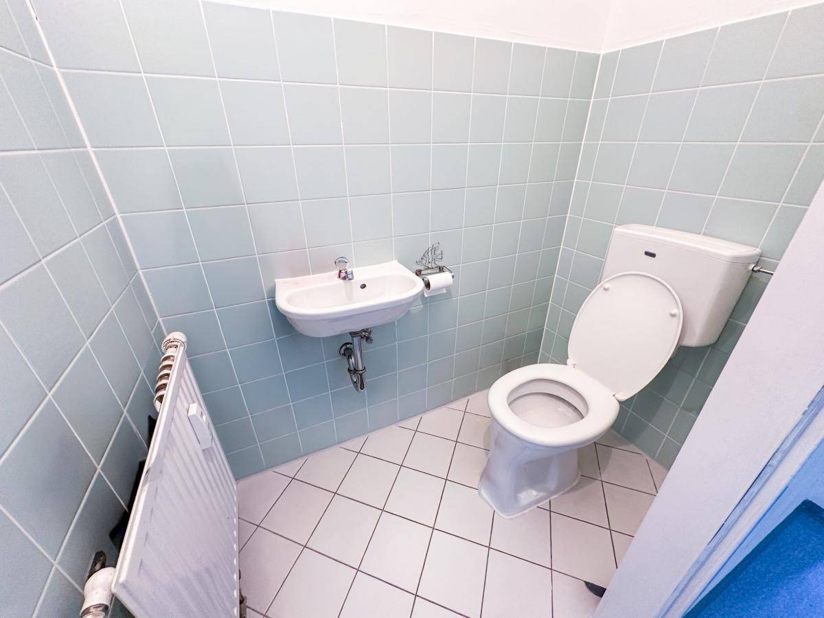 Kleines Gäste-WC mit hellblauen Fliesen, weißer Toilette und einem Waschbecken.
