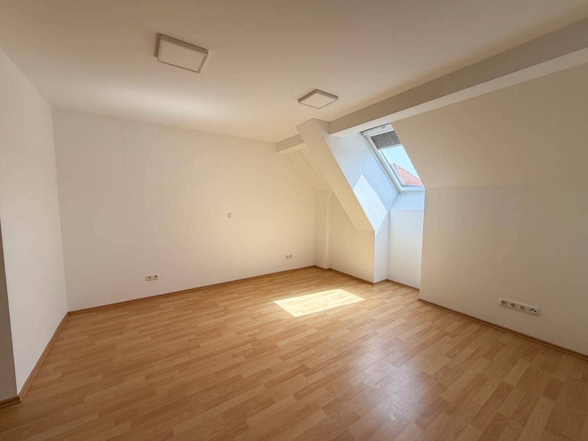 Helles Dachzimmer mit Laminatboden, Dachfenster und Heizkörper, ideal als Schlaf- oder Arbeitszimmer.