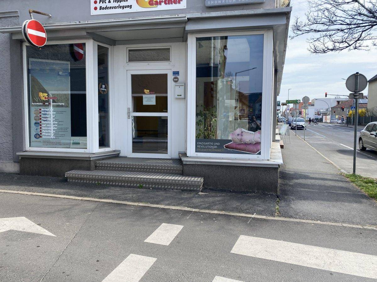 Eingangsbereich des Geschäfts mit Stufen, großen Schaufenstern und Blick auf die belebte Straße.