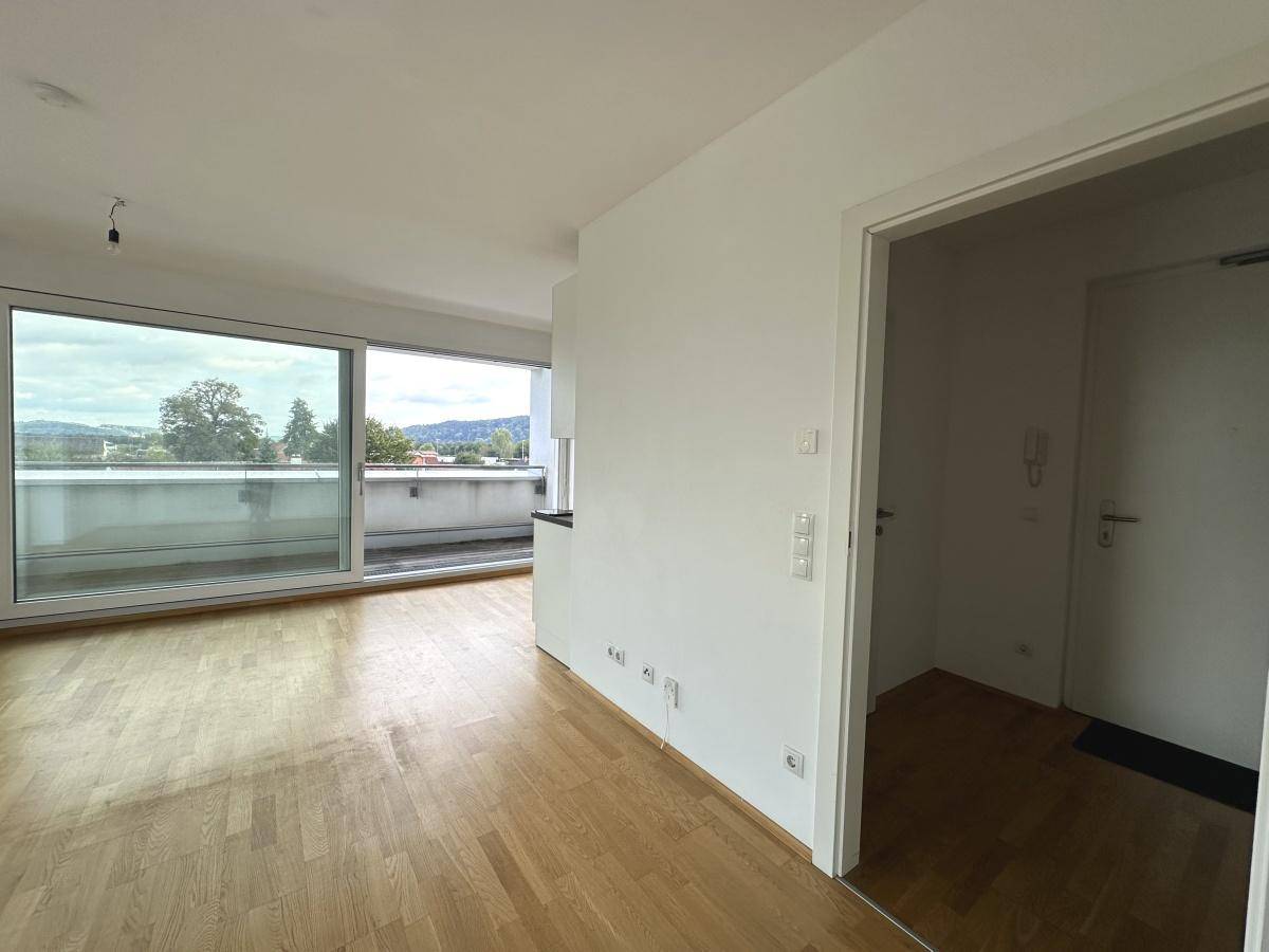 Blick vom Flur in den offenen Wohnbereich mit großen Fenstern und Zugang zum Balkon.