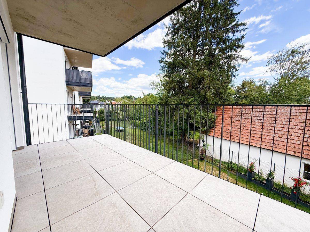Geräumiger Balkon mit Fliesenboden, schwarzem Geländer und Blick ins Grüne.