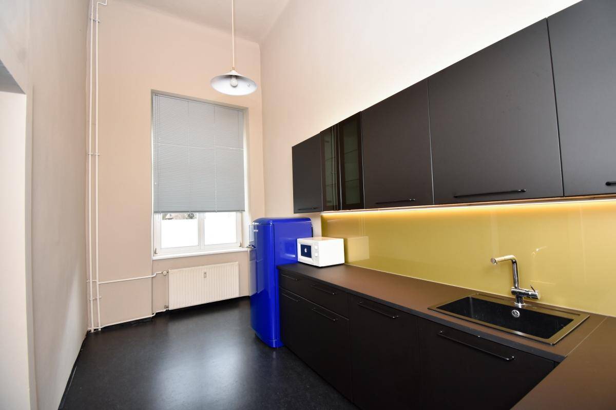 Moderne Küchenzeile mit dunklen Schränken, gelber Rückwand und einem blauen Retro-Kühlschrank neben einem Fenster.
