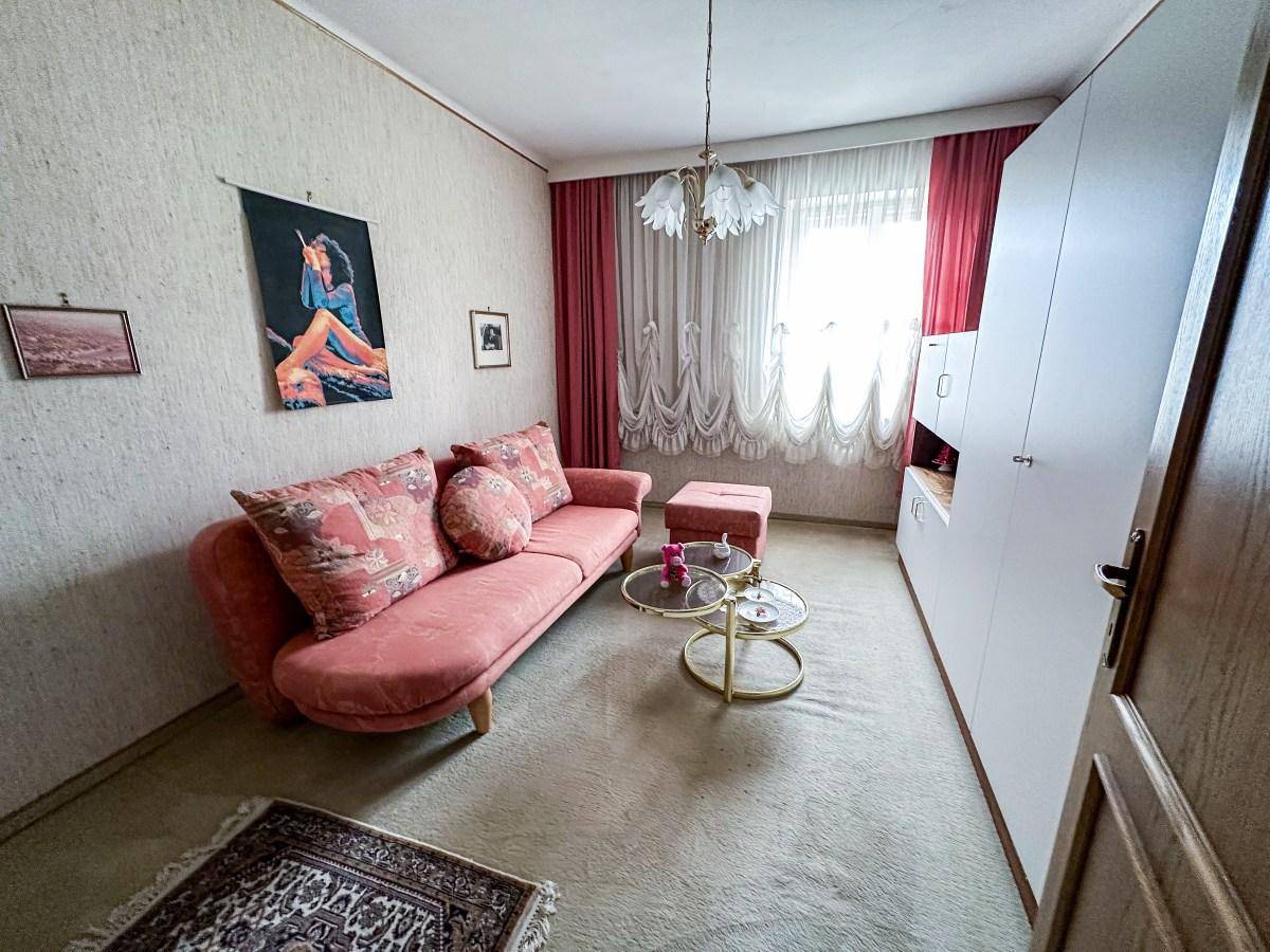 Wohnzimmer mit rosa Sofa, Teppichboden und großen Fenstern mit Vorhängen.