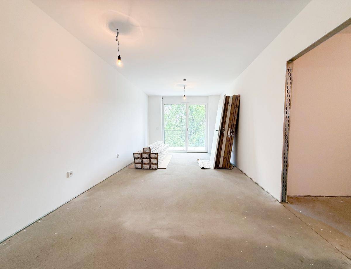Geräumiger Wohnbereich im Rohbau mit viel Tageslicht und Zugang zu einem Außenbereich.