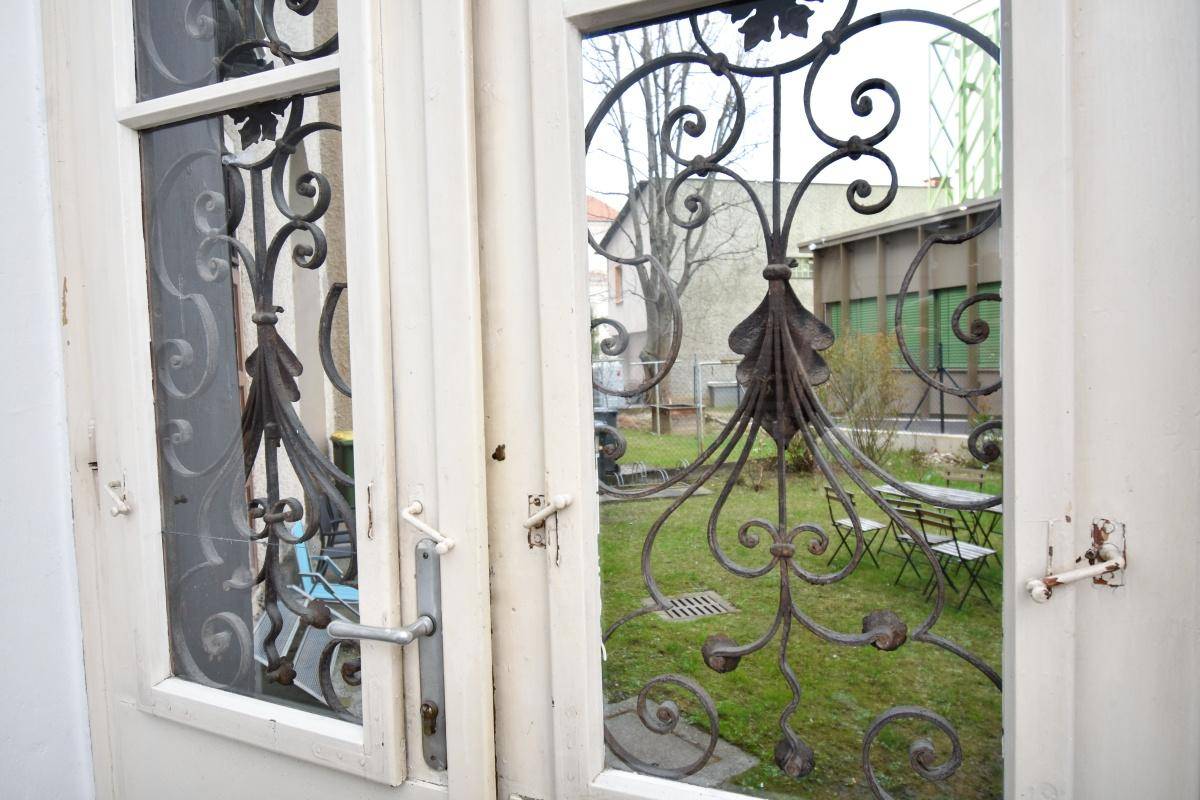 Detailansicht einer Tür mit schmiedeeisernen Verzierungen und Blick in den Garten.