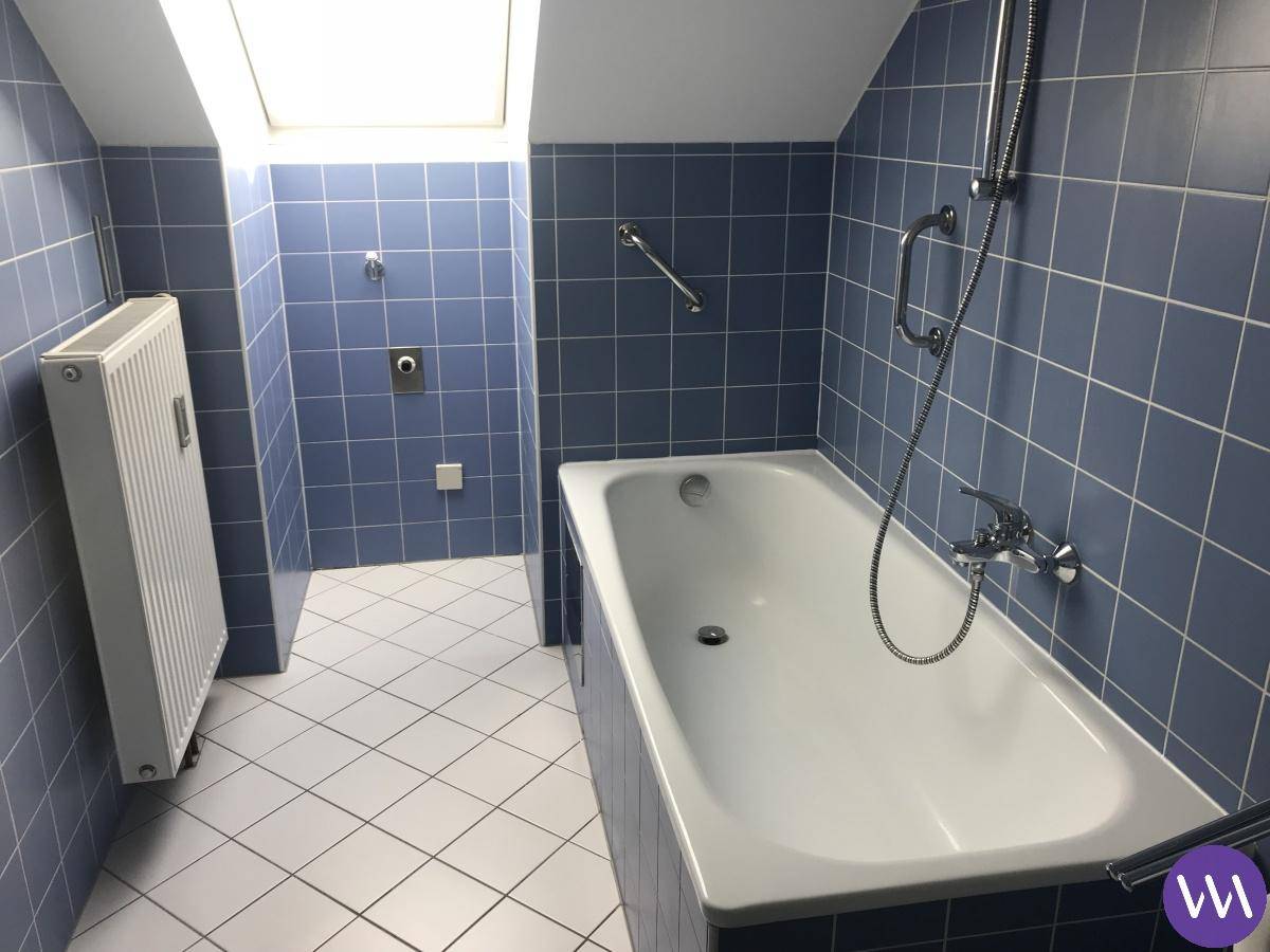 Badezimmer mit blauen Fliesen, Badewanne, Dachfenster und Heizkörper.