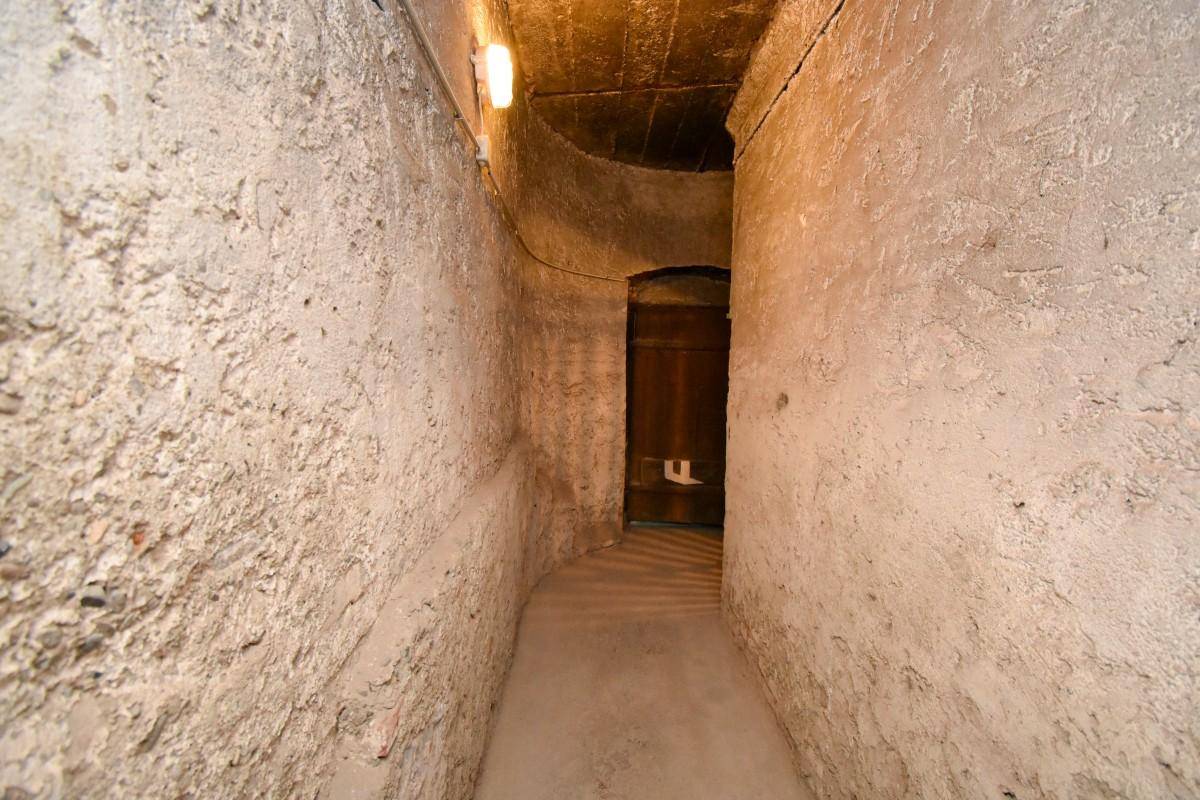 Sehr schmaler, gewölbter Kellergang mit rauen Wänden und begrenzter Beleuchtung.