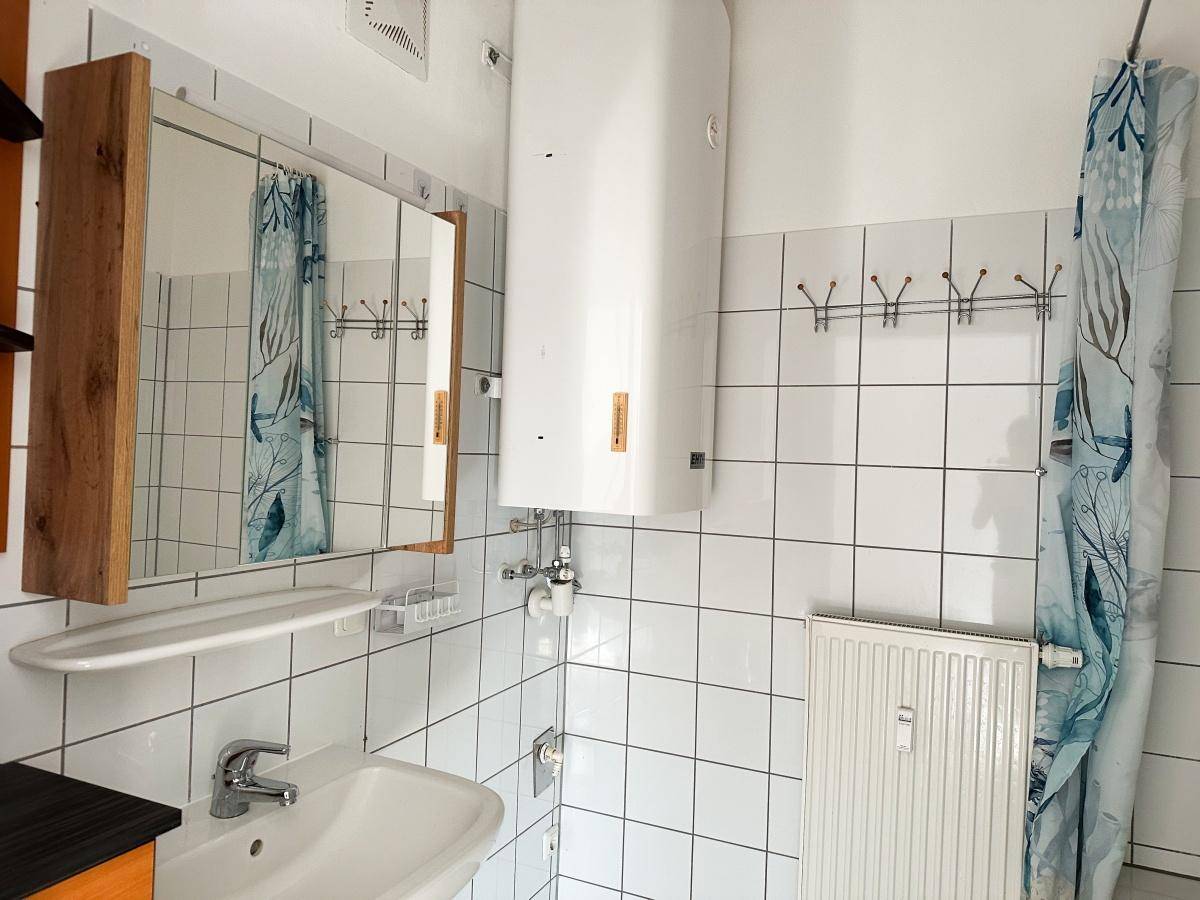 Badezimmer mit Badewanne, Waschbecken, weißen Fliesen und einem Warmwasserboiler.