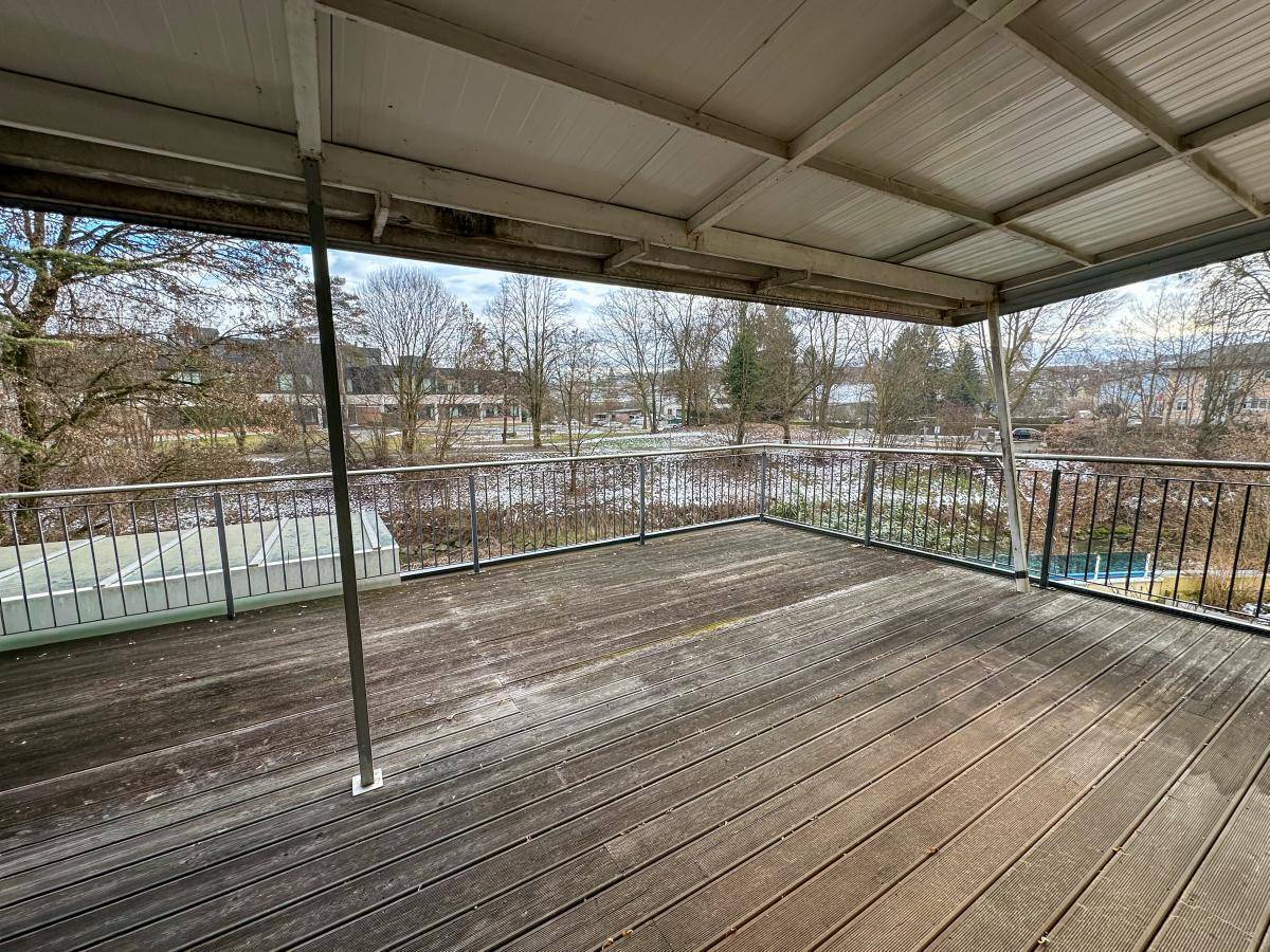 Großer überdachter Balkon mit Holzboden und weitem Blick ins Grüne.