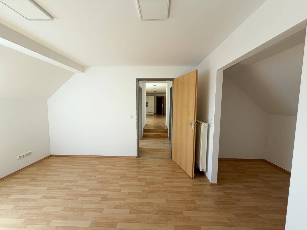 Heller Wohnbereich im Dachgeschoss mit Laminatboden und Zugang zu einem Flur oder Treppenhaus.