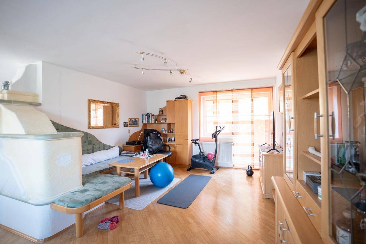 Geräumiges Wohnzimmer mit Kachelofen, Holzparkett und Fitnessgeräten.