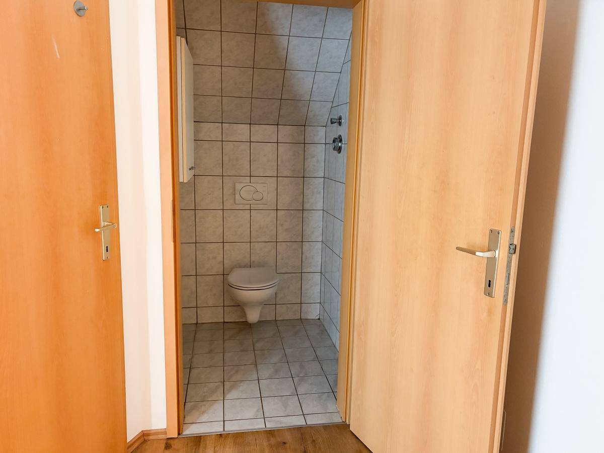 Kleines Gäste-WC mit gefliesten Wänden, Wand-WC und schräger Decke im Dachgeschoss.