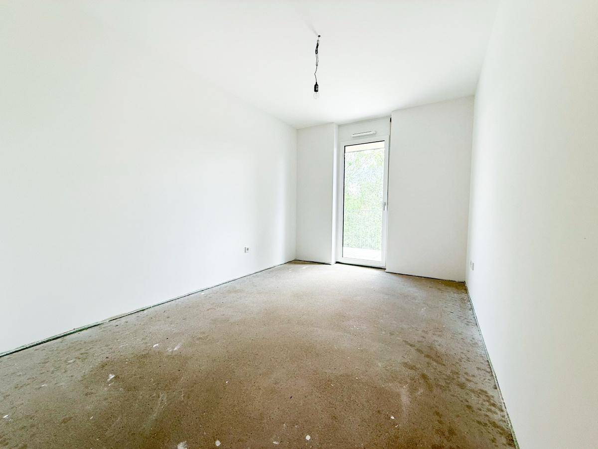 Helles Zimmer im Rohbau mit großen Fenstern und weiß gestrichenen Wänden.