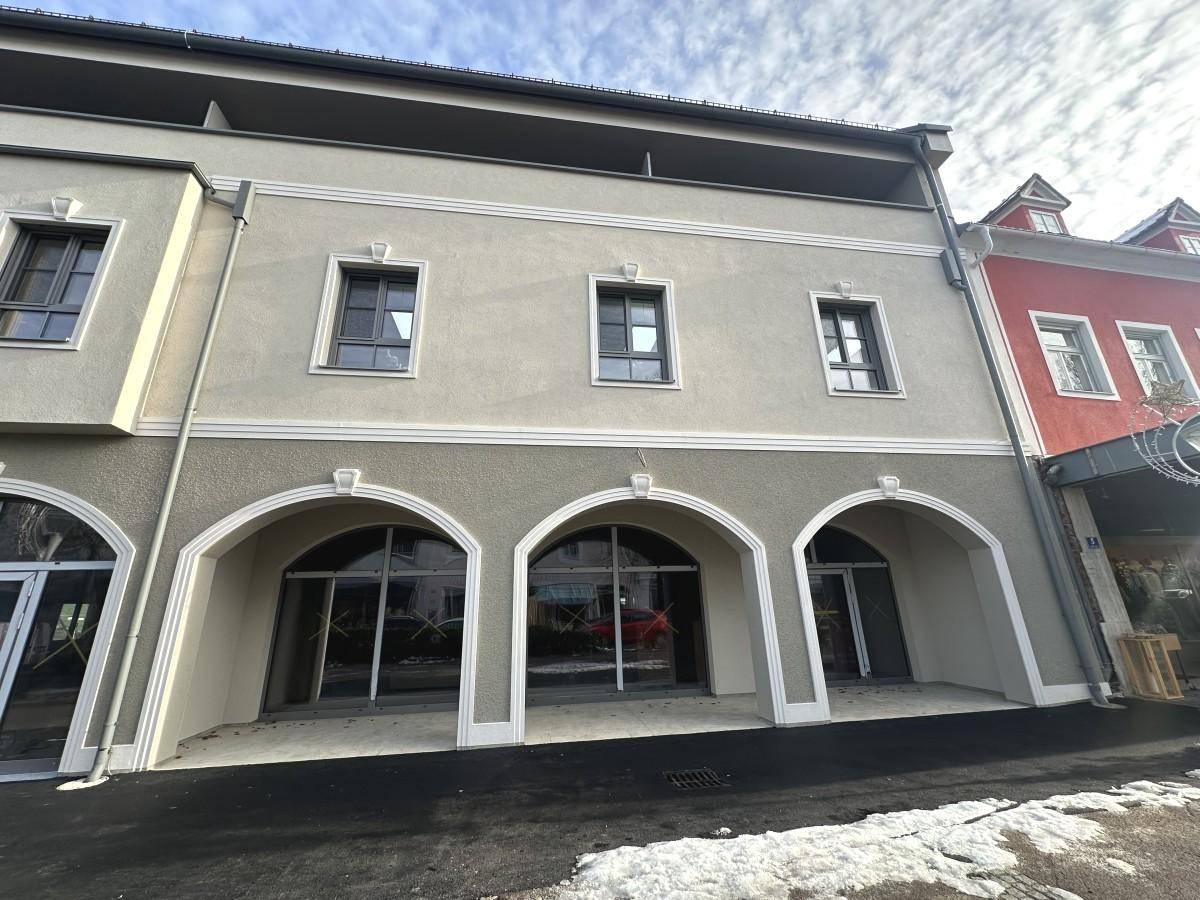 Außenansicht eines modernen Gebäudes mit markanten Bogenfenstern im Erdgeschoss und einer hellen Fassade.