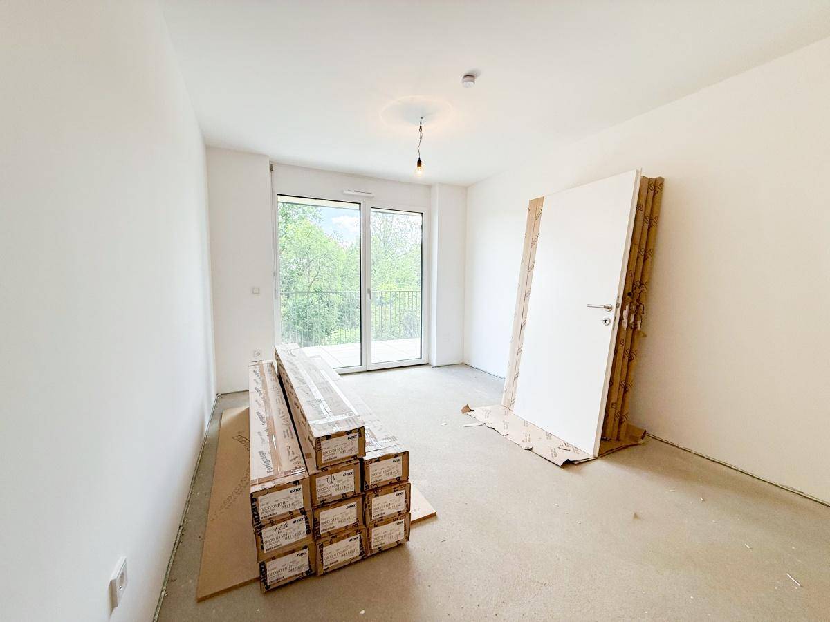 Unfertiger Raum mit großen Fenstern und Zugang zum Balkon, Baumaterialien liegen bereit für den Innenausbau.