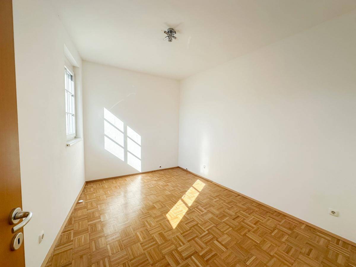 Freundliches Zimmer mit Parkettboden und einem Fenster, das den Raum mit Licht erfüllt.