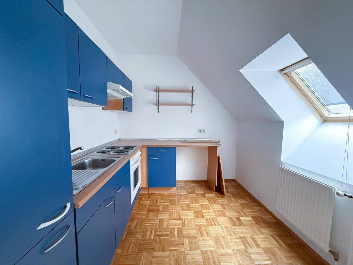 Funktionale Küche mit blauen Schränken, Herd, Spüle und einem Dachfenster in einem Raum mit Dachschräge.