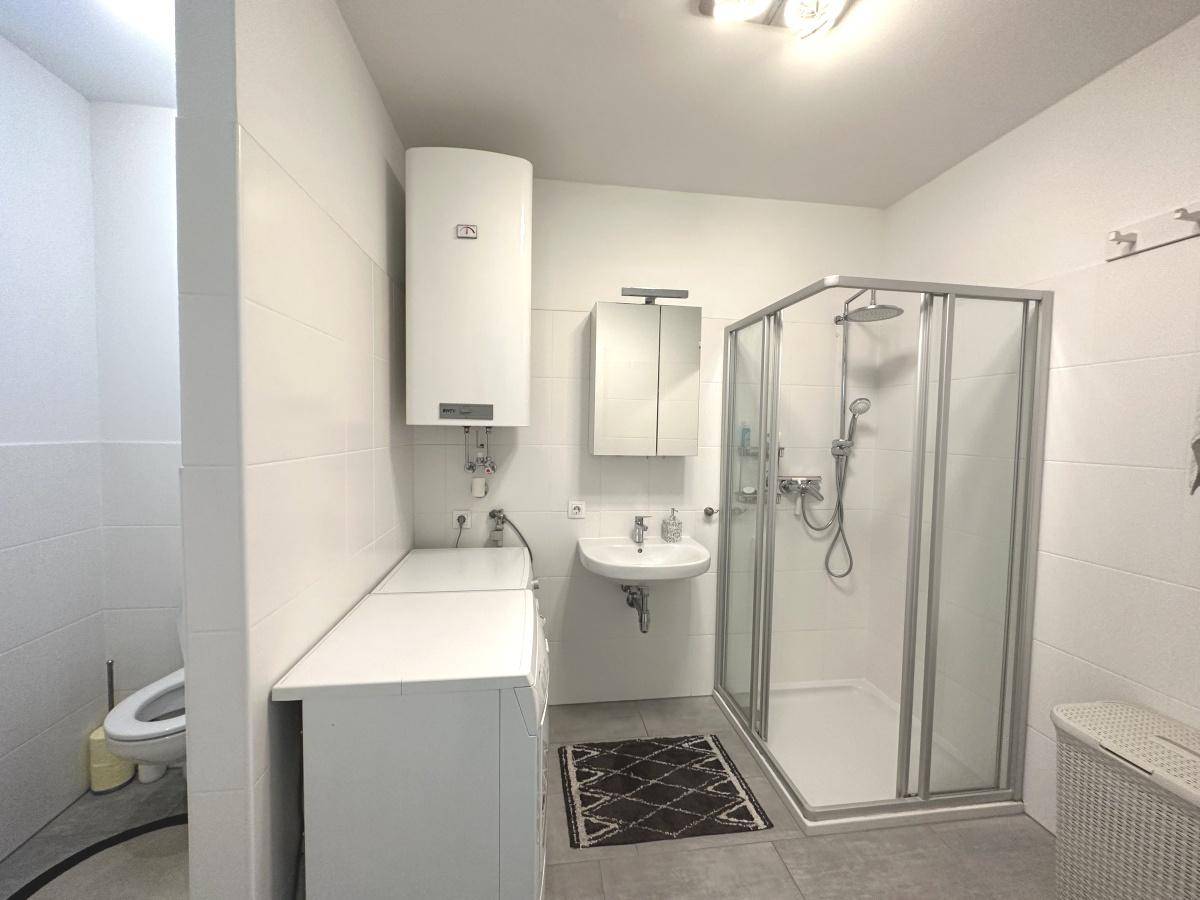 Helles Badezimmer mit Duschkabine, Waschbecken und separatem WC-Bereich.