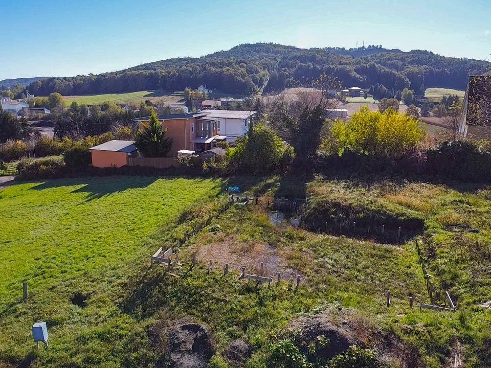 Sonnige Luftaufnahme eines großen Grundstücks mit viel Grün, einem kleinen Teich und Fernblick auf bewaldete Hügel.