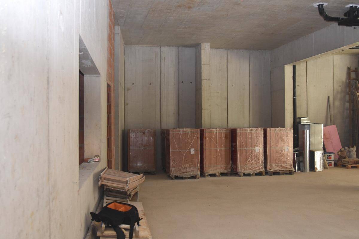 Rohbau eines Gewerberaums mit hohen Betonwänden, einem kleinen Fenster und gestapelten Baustoffen.