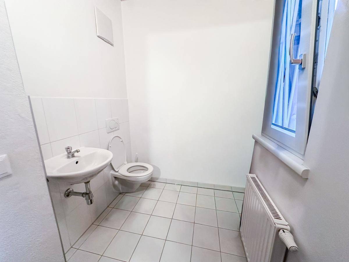Helles Gäste-WC mit Fenster, weiß gefliesten Wänden und einem Waschbecken.