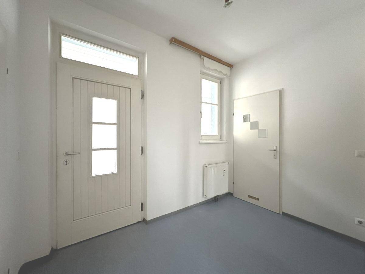 Eingangsbereich mit strapazierfähigem Bodenbelag, weißer Tür und einem kleinen Fenster.